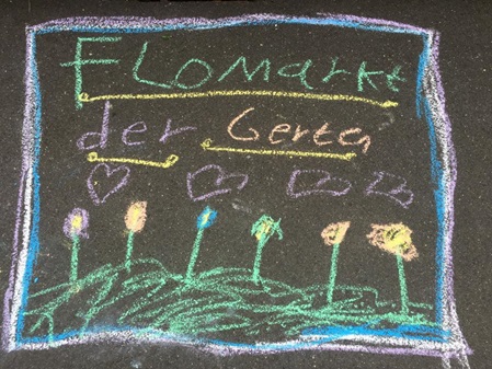 Mit bunter Kredse von Kindern auf einer dunkelgrauen Gehwegplatte ein lila Quadrat gemalt wo in bunt drin steht: Flohmarkt der Gerten darunter 4 Herzen und darunter 6 bunte Blumen auf einer grünen Wiese.
